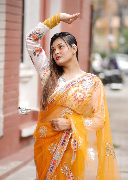Woman in a yellow saree with floral patterns standing outdoors.