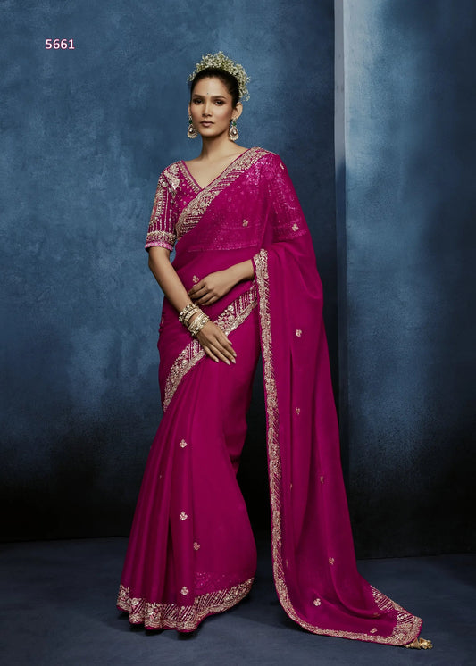 Woman wearing a vibrant pink saree with gold embroidery against a dark blue background