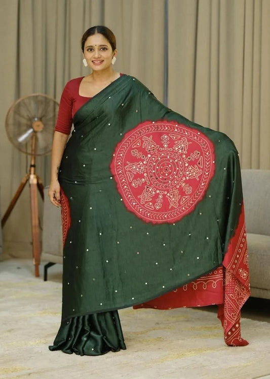 Woman wearing a green saree with a red border and intricate design, standing indoors.
