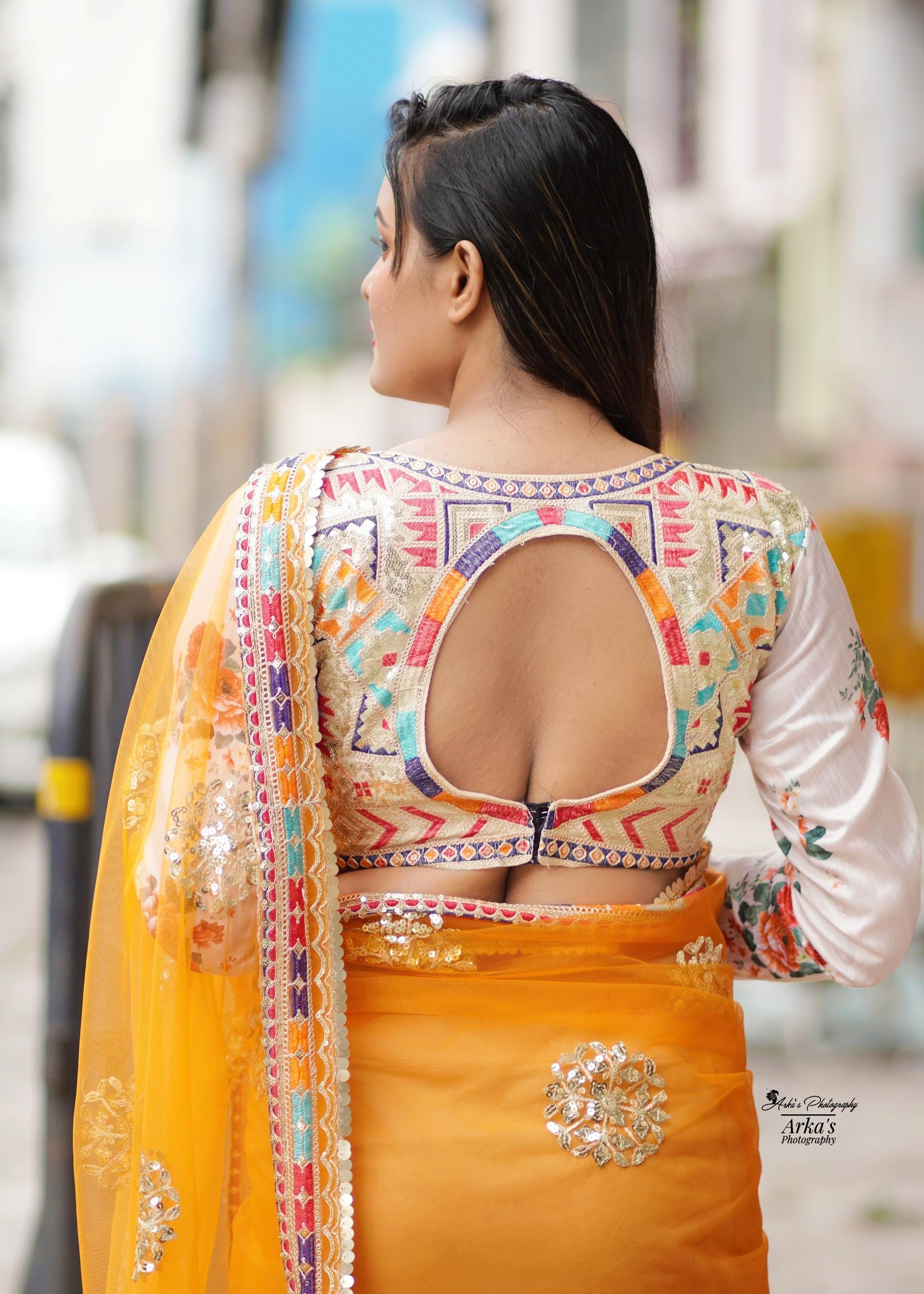 Woman wearing a traditional orange saree with a colorful blouse in an urban setting