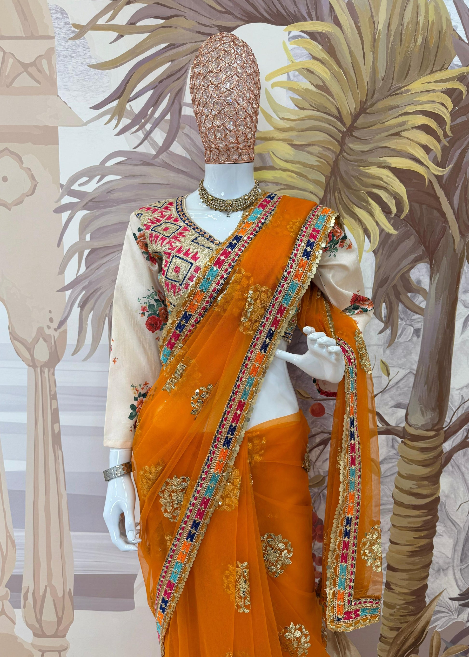 Mannequin wearing an orange saree with intricate patterns against a decorative background
