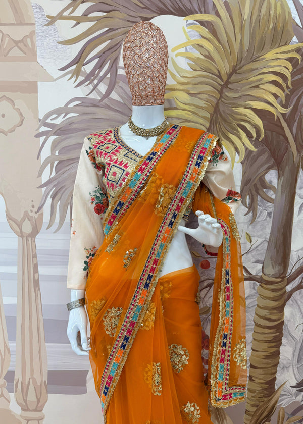 Mannequin wearing an orange saree with intricate patterns against a decorative background