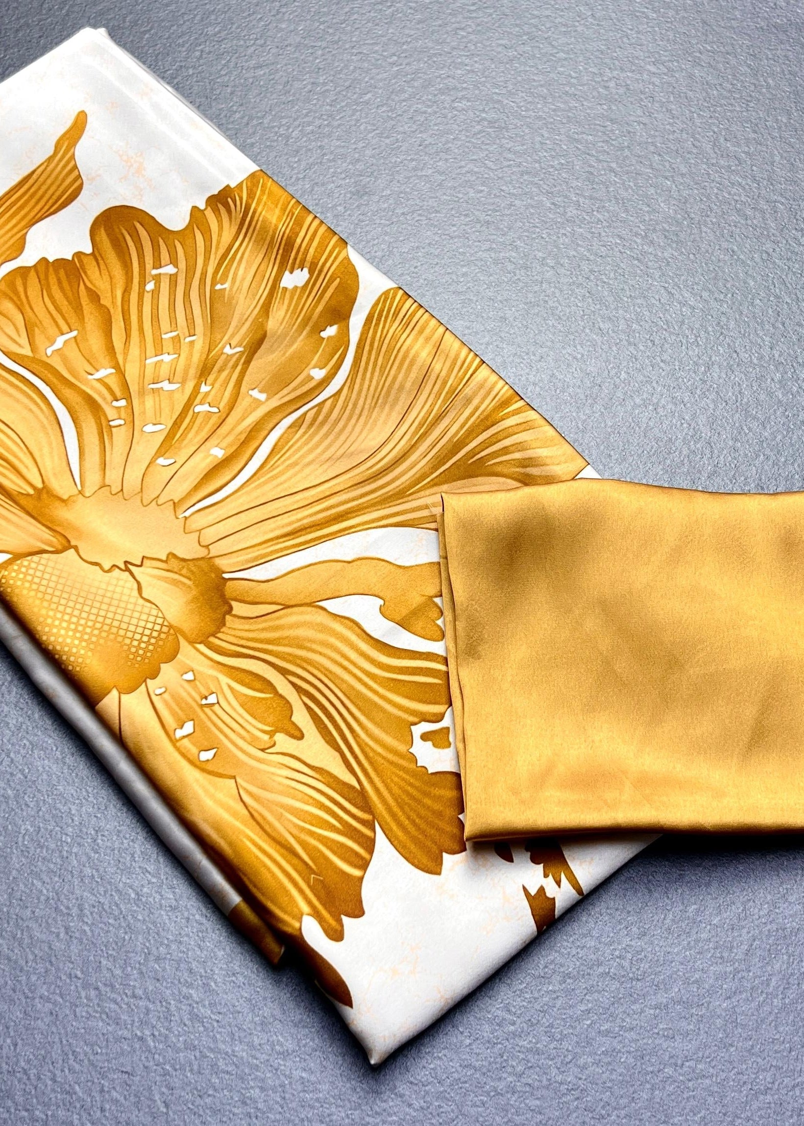 Gold floral-patterned fabric on a white background with a gold square fabric piece beside it.