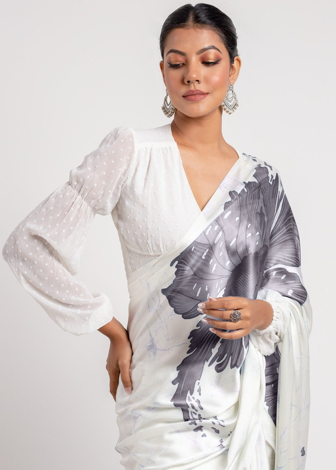 Woman wearing a white saree with black floral patterns on a plain background
