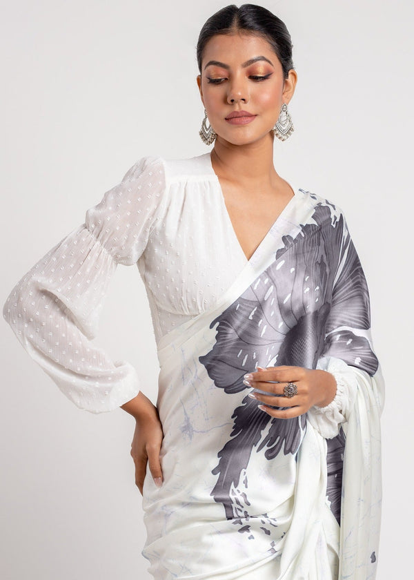 Woman wearing a white saree with black floral patterns on a plain background