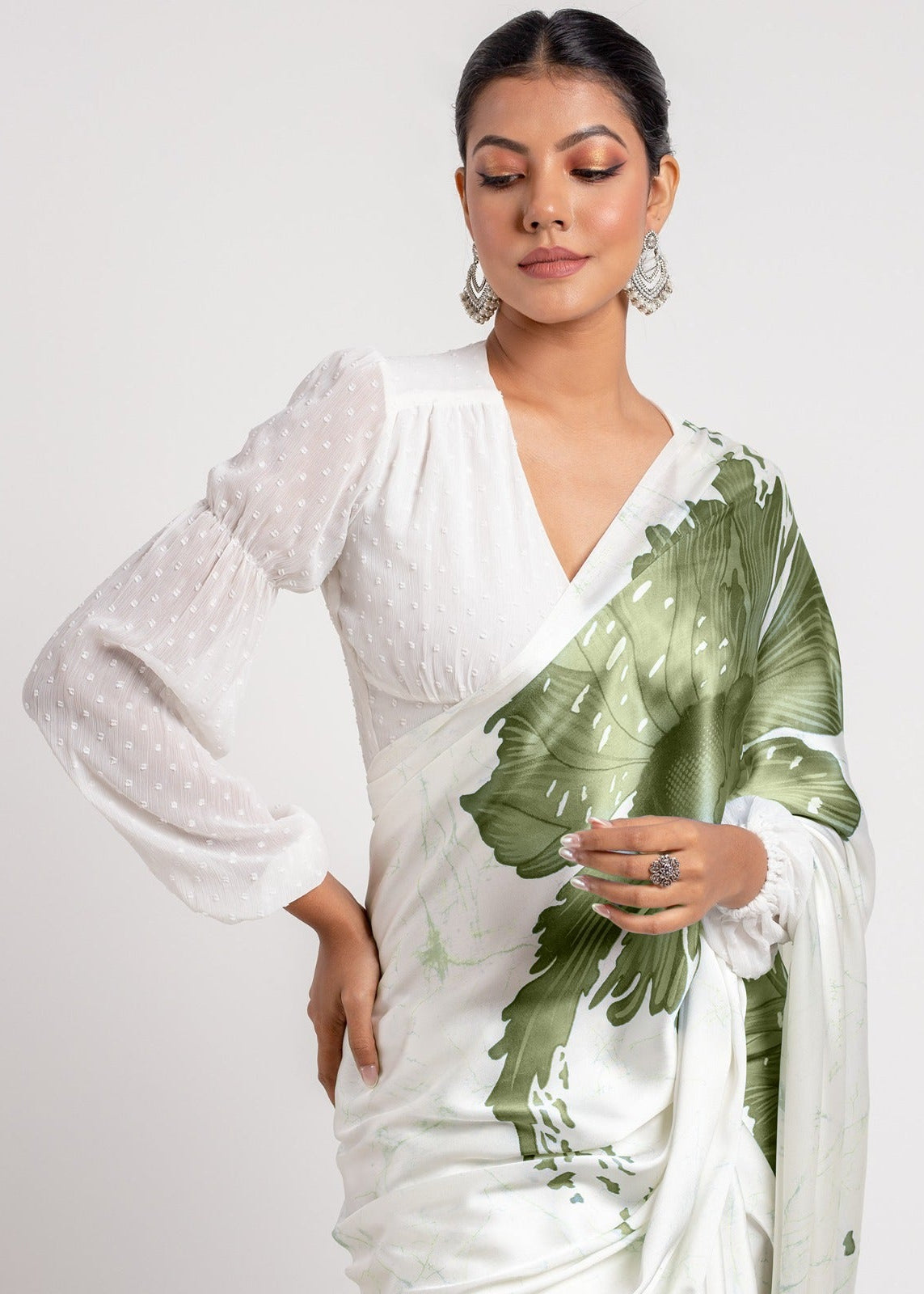 Woman wearing a white saree with green leaf patterns on a plain background