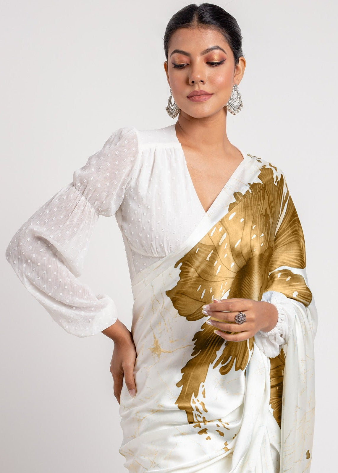 Woman wearing a white saree with gold patterns on a plain background