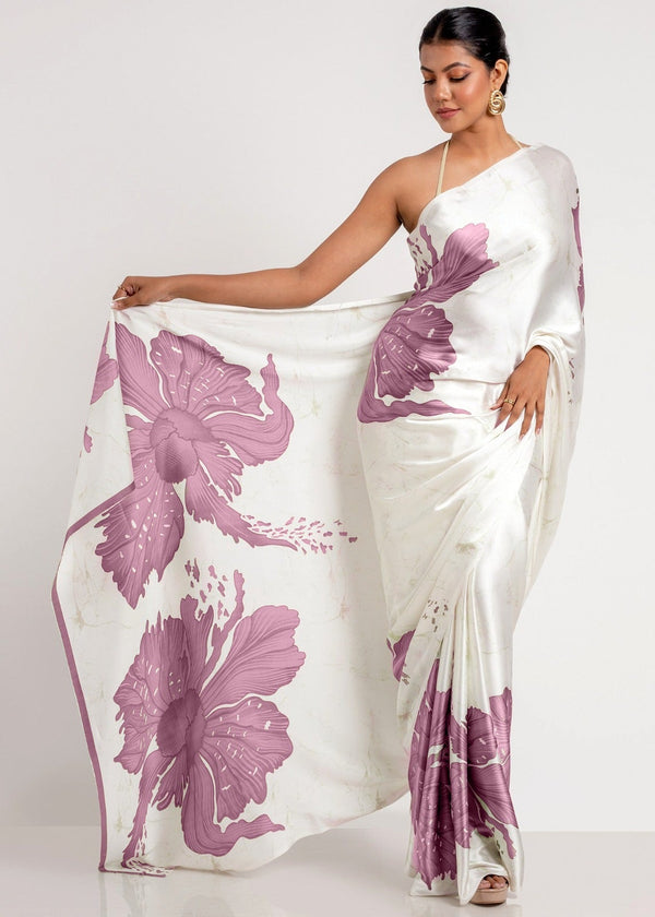 Woman wearing a white saree with purple floral patterns on a plain background