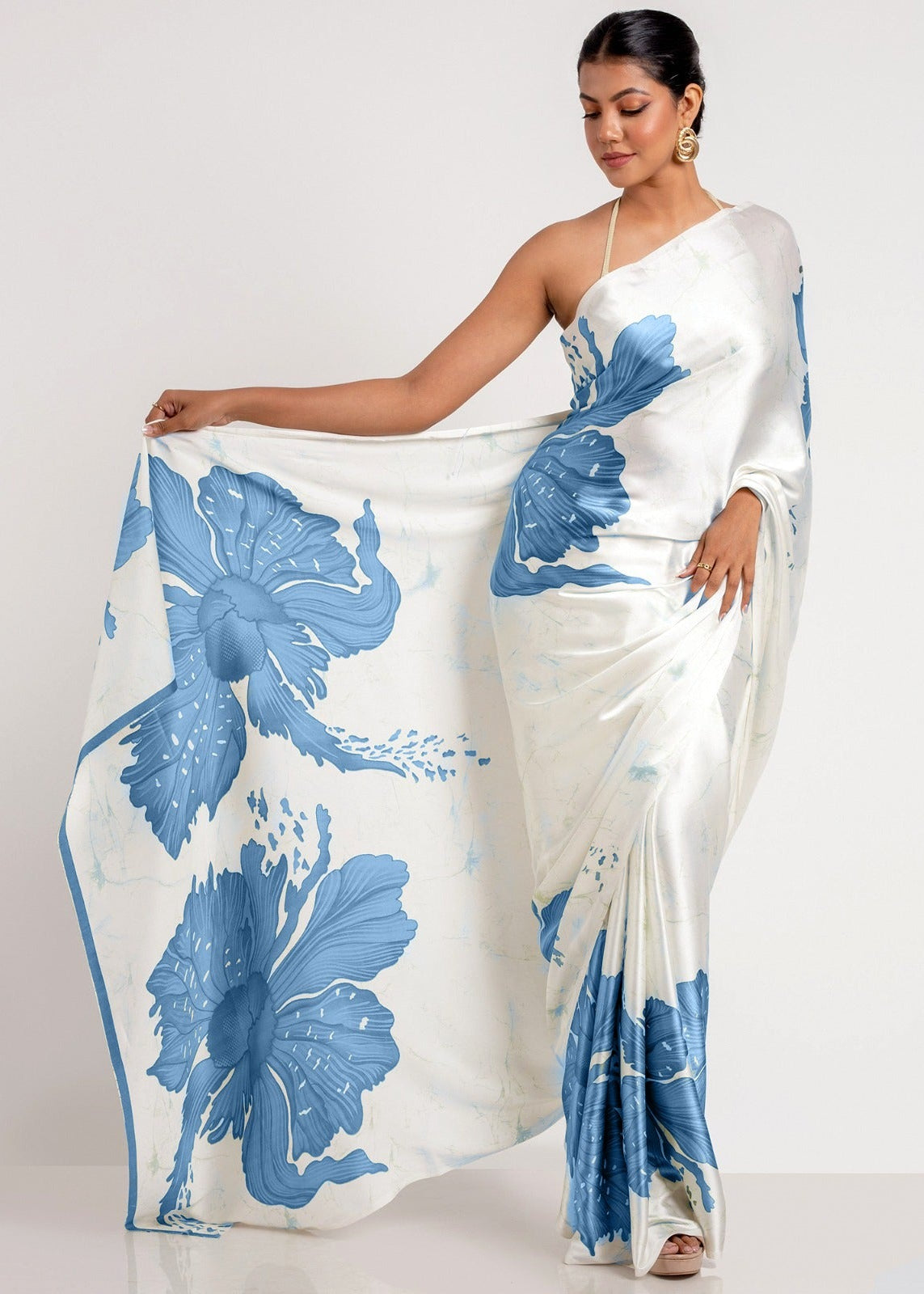 Woman wearing a white saree with blue floral patterns on a plain background