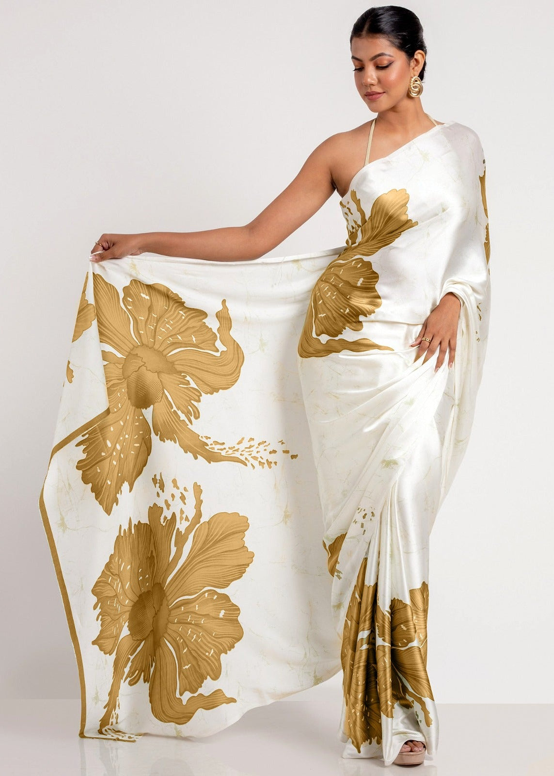Woman wearing a white saree with gold floral patterns on a plain background