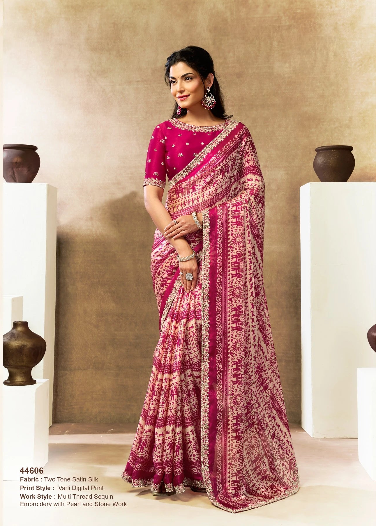 Woman wearing a pink saree with traditional patterns in an indoor setting.