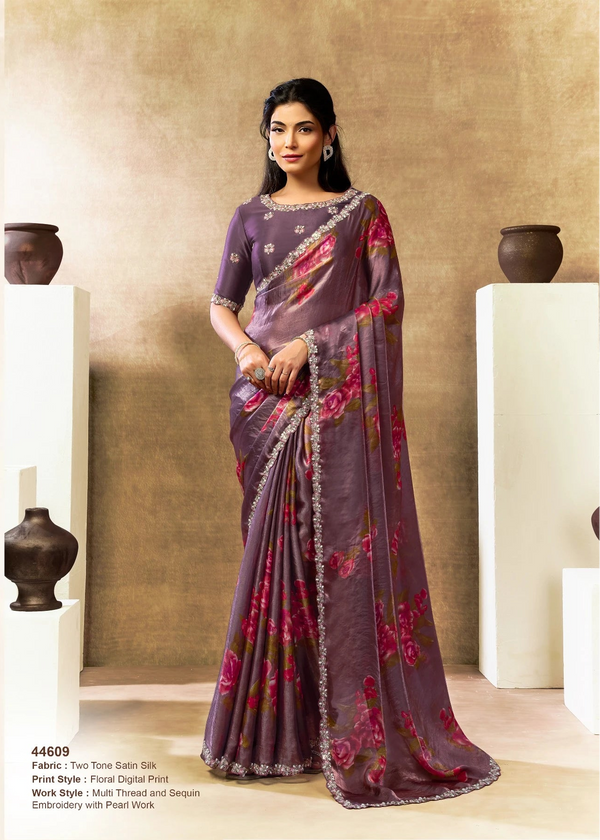 Woman wearing a purple saree with floral patterns in an indoor setting.
