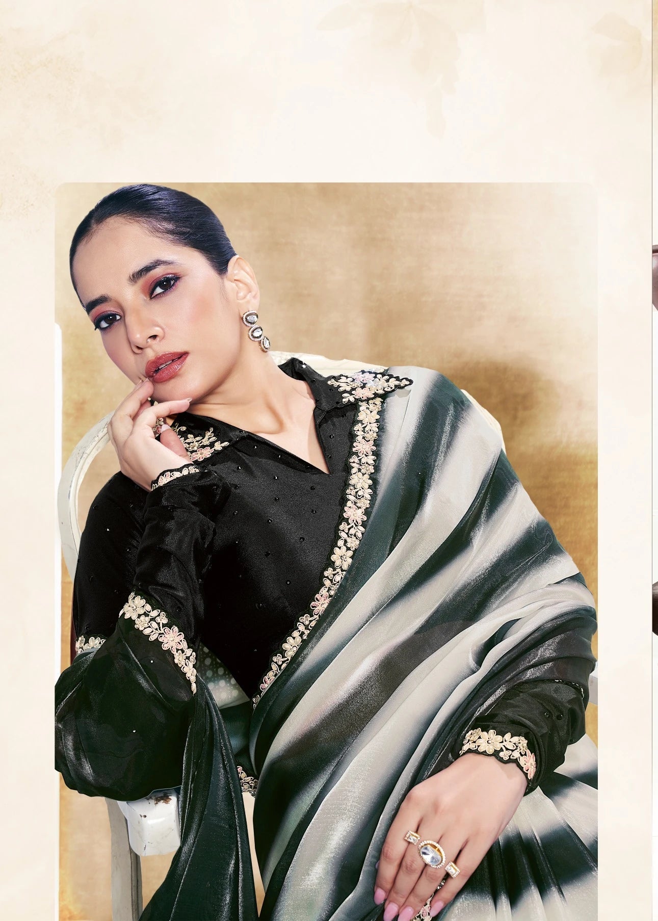 Woman wearing a black and white saree with a gold border, posing indoors.