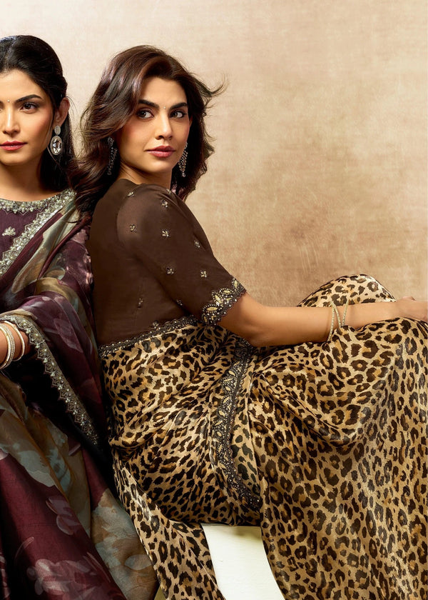Two women wearing traditional sarees with a focus on one in leopard print against a beige background.