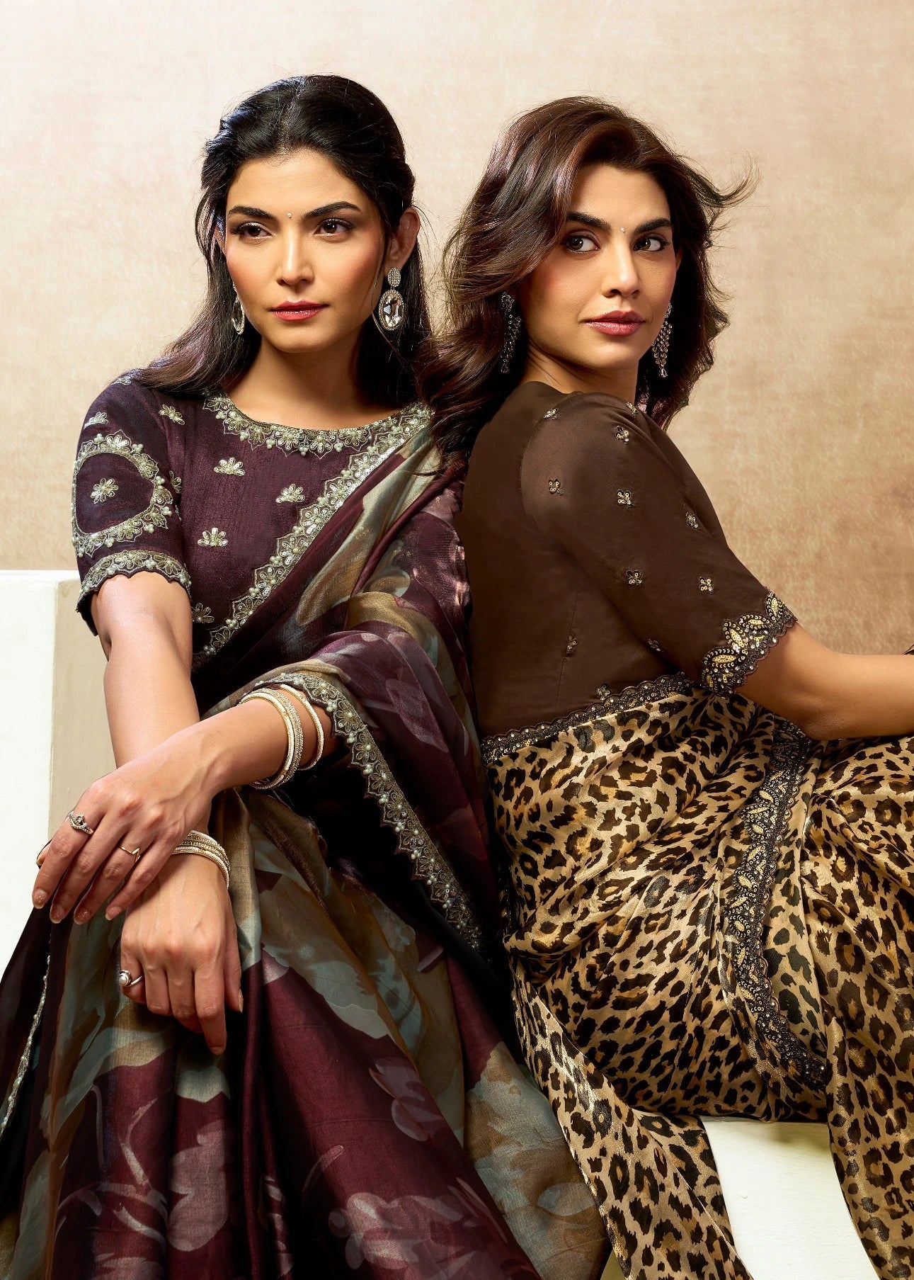 Two women wearing traditional sarees with a focus on one in leopard print against a beige background.
