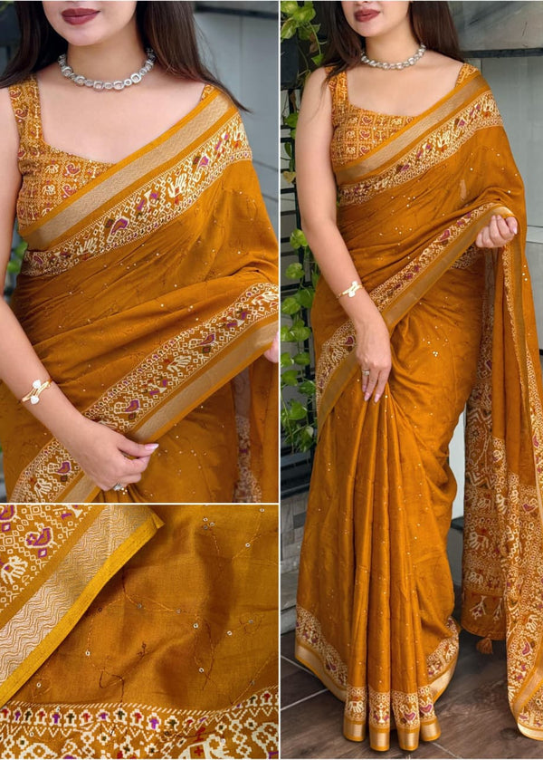 Woman wearing a mustard yellow saree with intricate patterns, standing indoors.