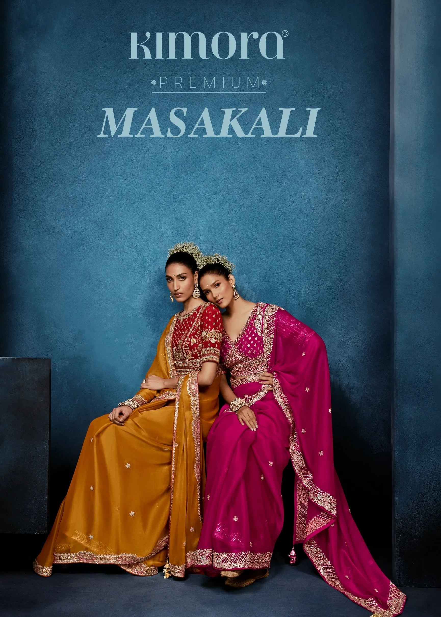 Two women in traditional sarees sitting against a blue background with 'Kimora Premium Masakali' branding.