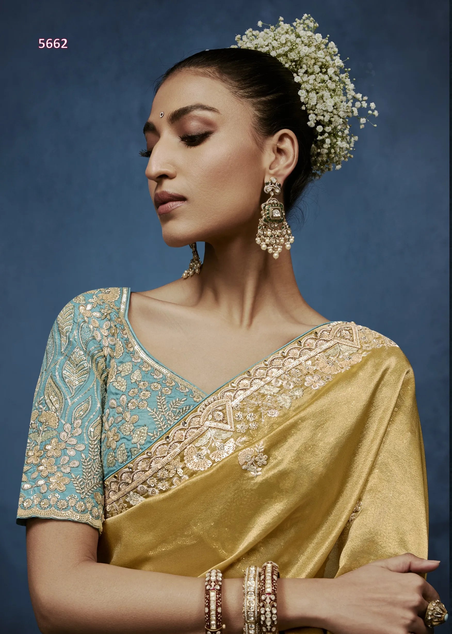 Woman wearing a gold and blue saree with intricate patterns against a dark background