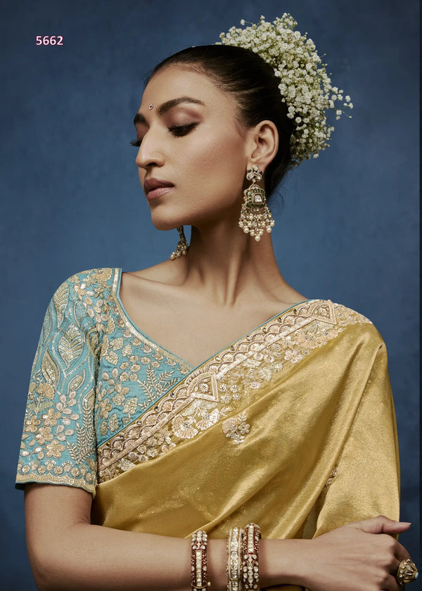 Woman wearing a gold and blue saree with intricate patterns against a dark background