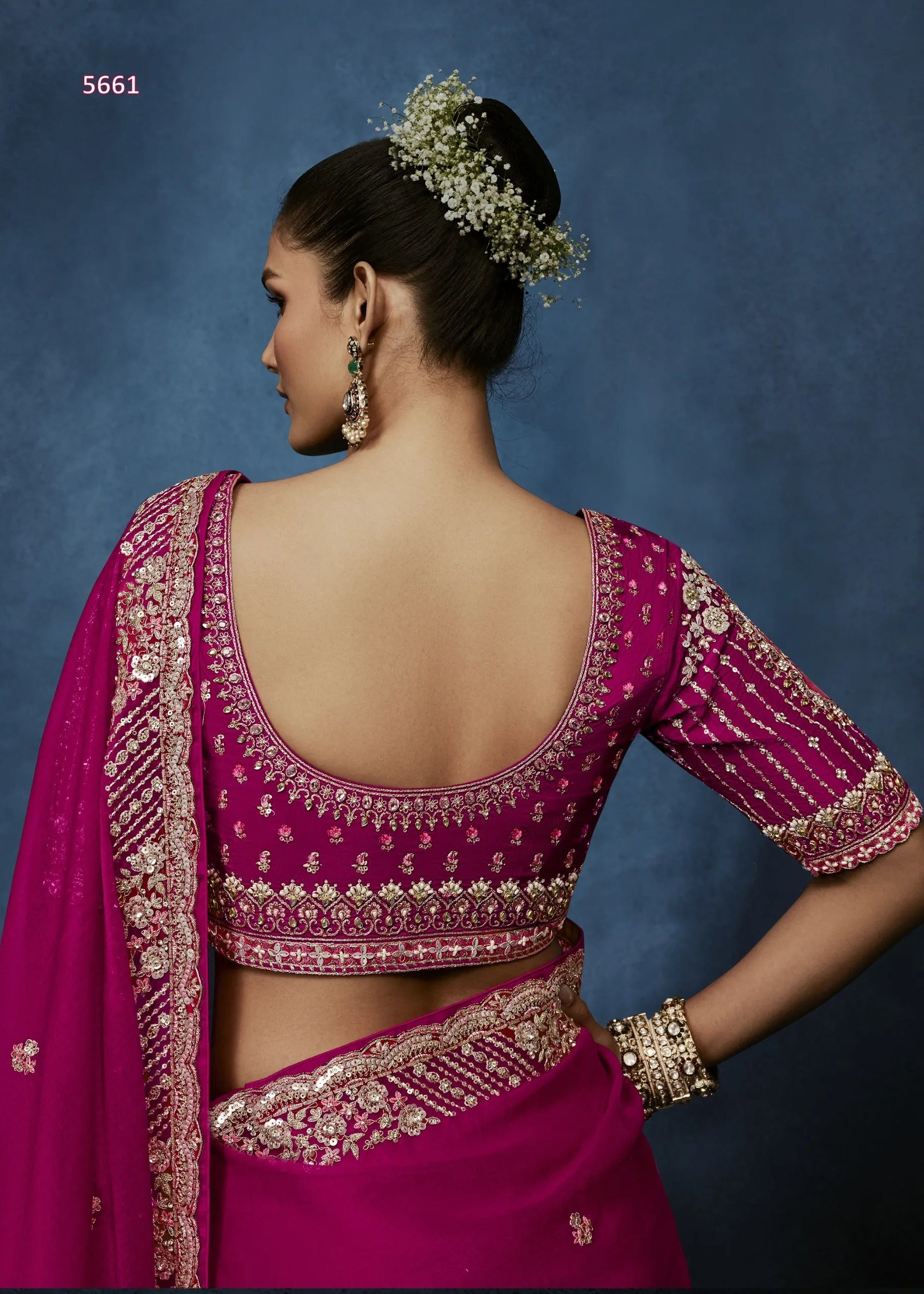 Woman wearing a pink saree with gold embroidery against a blue background