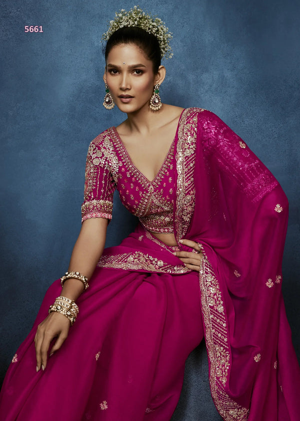Woman wearing a vibrant pink traditional outfit with gold embroidery against a blue background