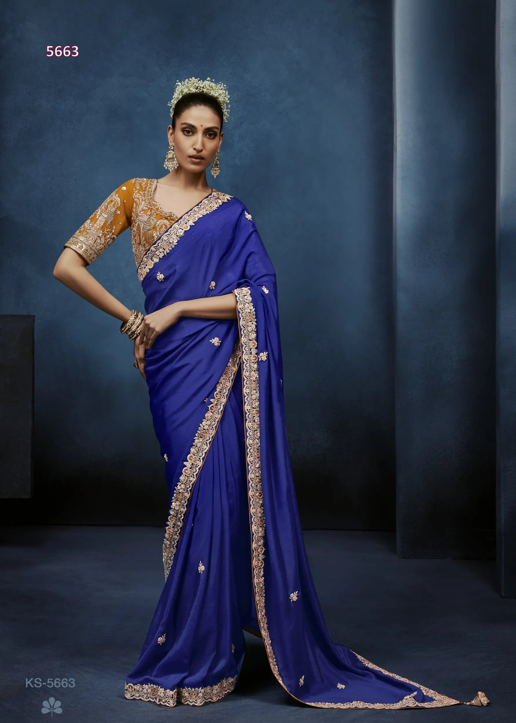 Woman wearing a blue saree with gold border against a dark background