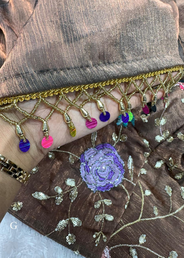 Close-up of a brown fabric with gold fringe and colorful tassels, featuring a purple flower design.
