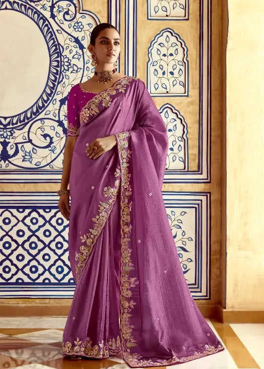 Woman in a purple saree with gold embroidery against a decorative wall.