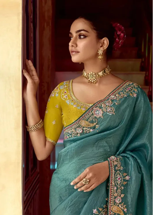 Woman in a teal saree with gold embroidery in an elegant interior setting
