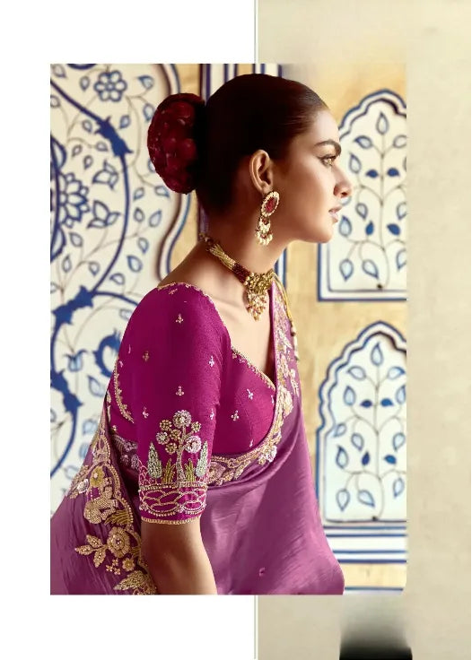 Woman in a purple saree with gold embroidery against a decorative wall.