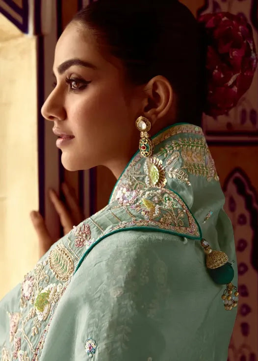 Woman in a light blue saree with green blouse standing in a decorated room.