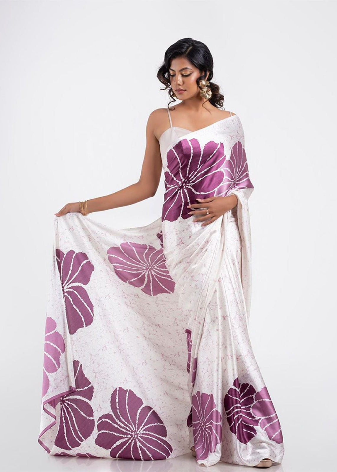 Woman wearing a white saree with purple floral patterns on a white background