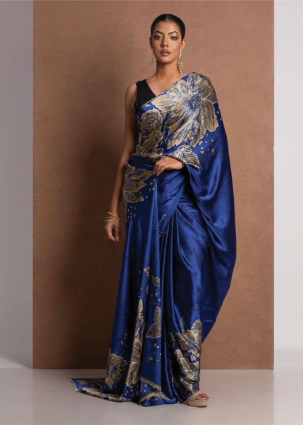 Woman wearing a blue saree with gold patterns against a brown background