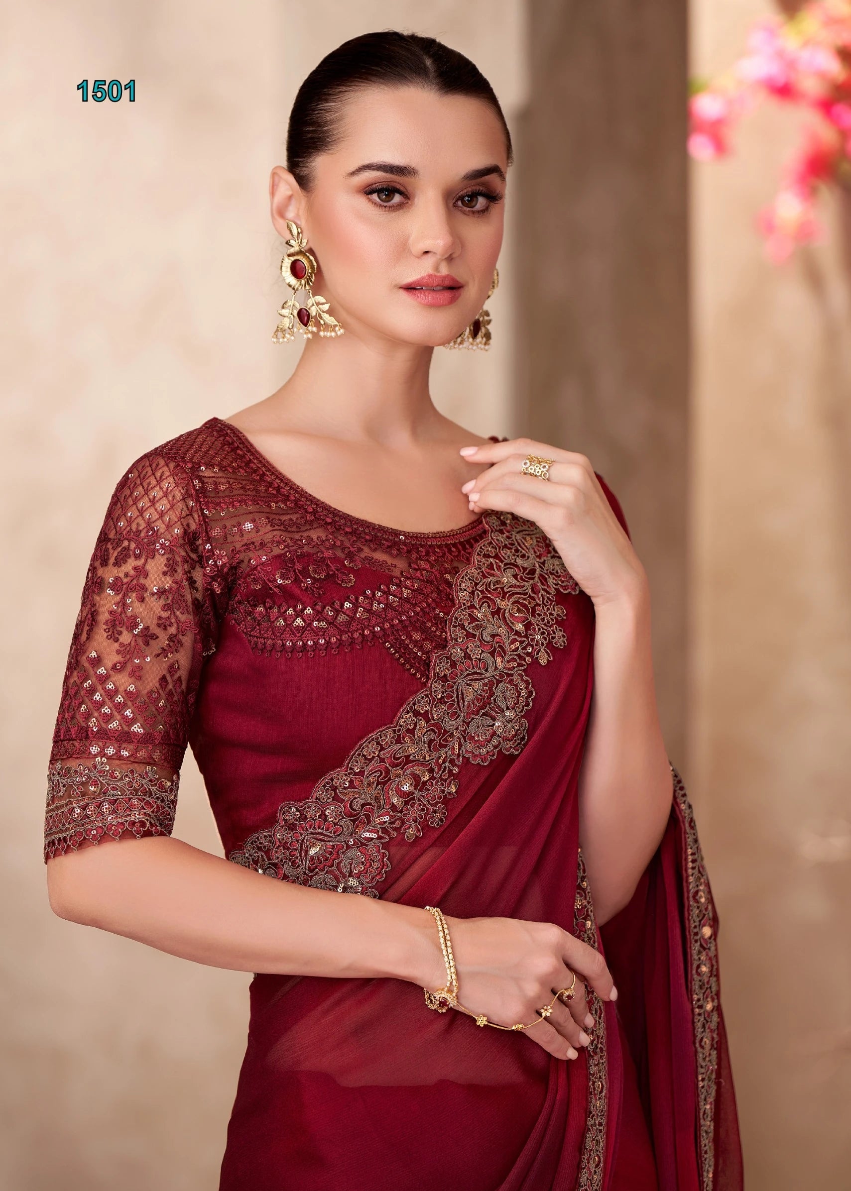 Woman wearing a maroon saree with gold embroidery against a beige background